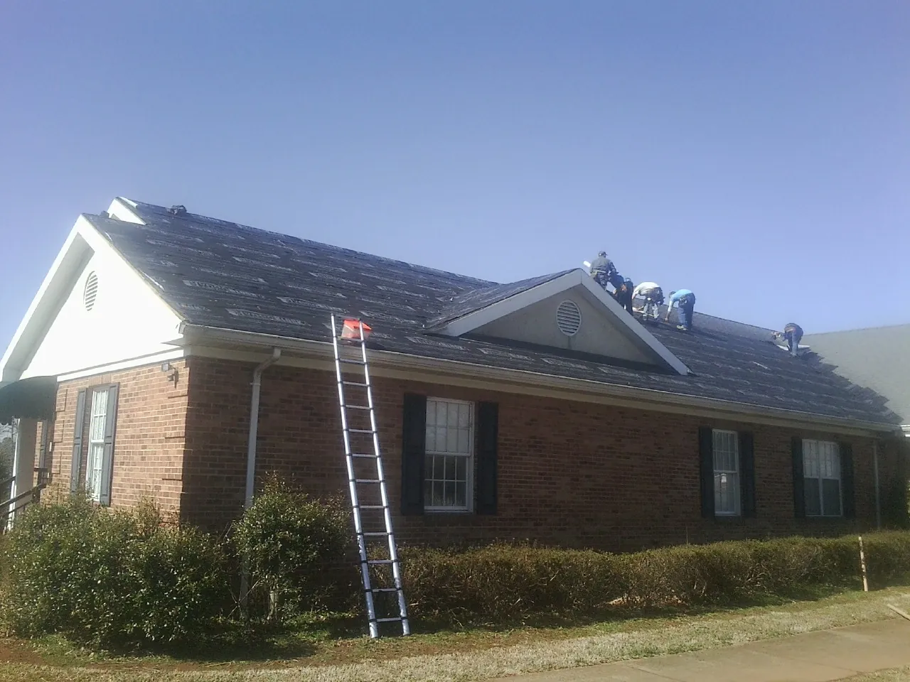 Crew tearing shingles off a brick ranch roof with a ladder set — Emergency Roof Repair work by our crew in Ellicott City
