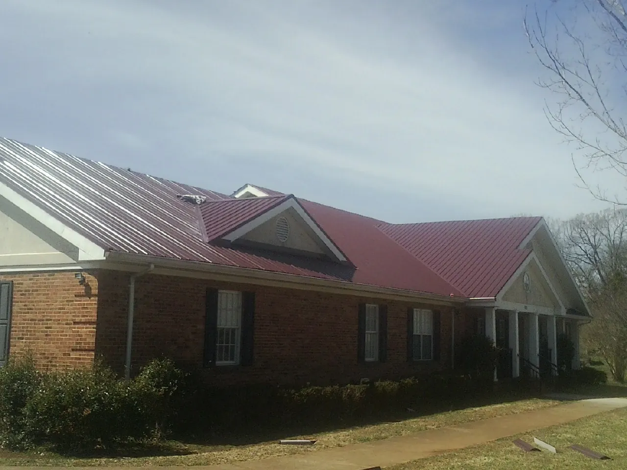 Red metal roof with gabled entries on a long brick building, from a Hail Damage Roof Repair job in Ellicott City