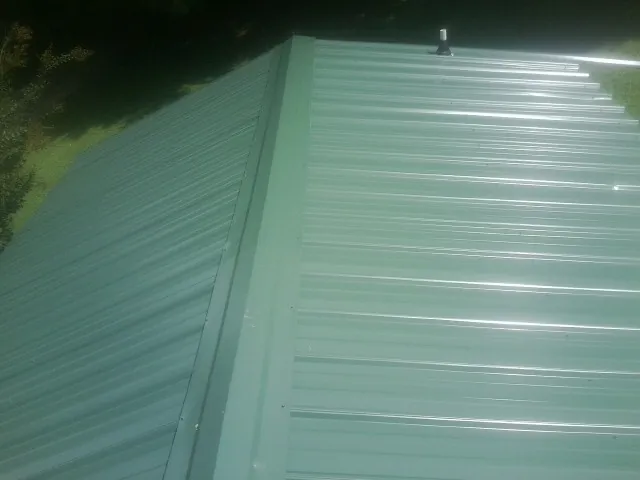 New green metal panels meeting at the ridge of a roof — Flat Roof Repair work by our crew in Ellicott City