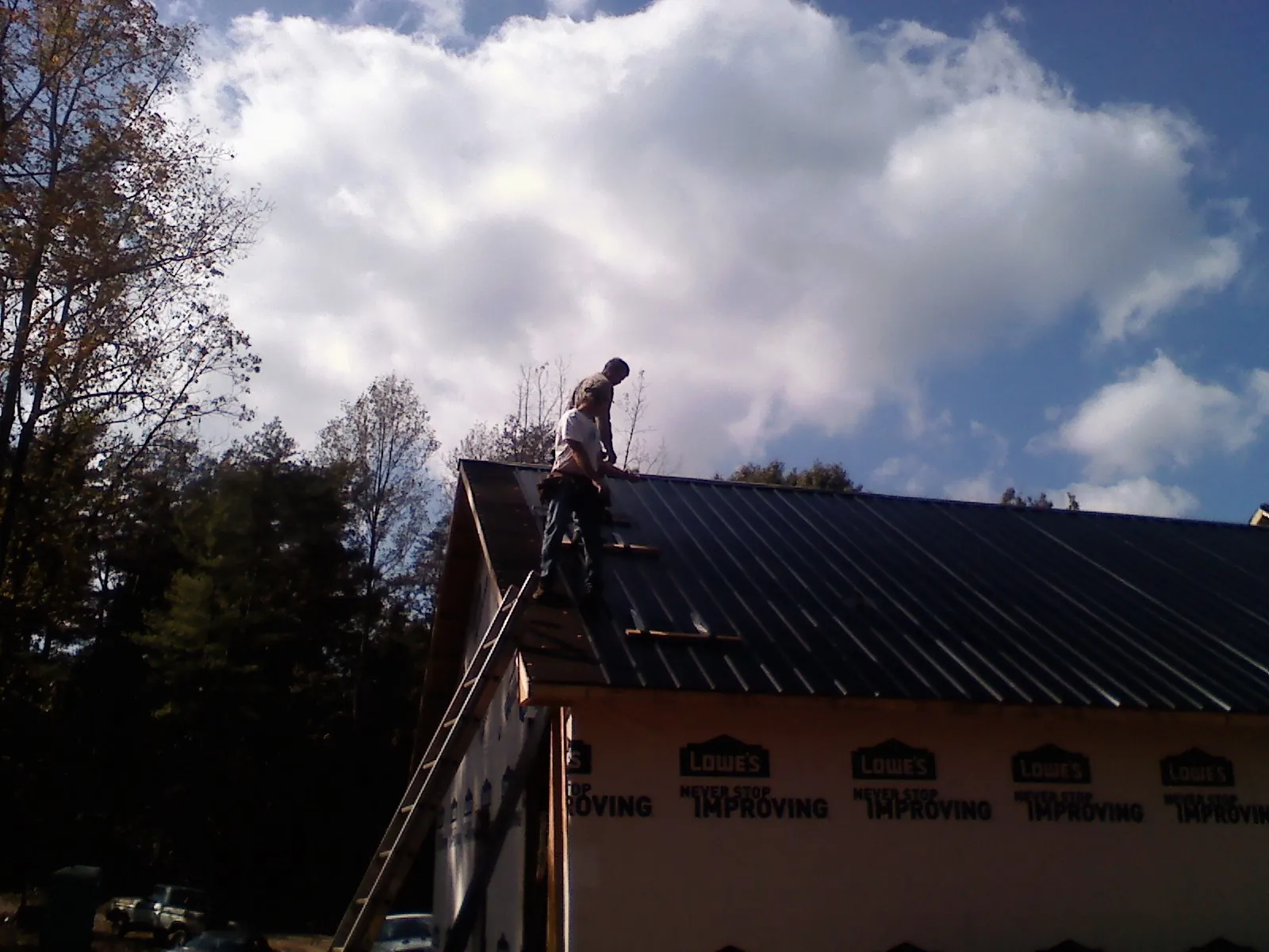 Roofer fastening dark metal panels high against a cloudy sky, from a Roof Inspection job in Ellicott City