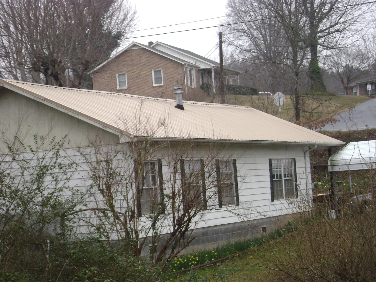 Tan metal roof on a white sided house set into a hillside — Commercial Roofing by Roofing Brothers in Ellicott City